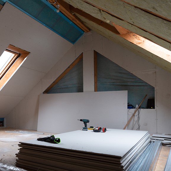 Image of a loft conversion taking place, a drill lies on a pile of plasterboard.